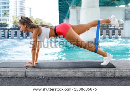 Fitness woman doing exercise for glutes with resistance band outdoors. Athletic girl workout