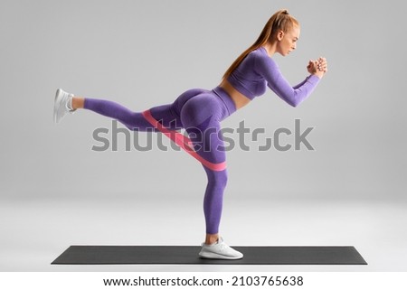 Fitness woman doing exercise for glutes with resistance band on gray background. Athletic girl working out
