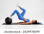 Fitness woman doing glute bridge exercise with med ball on gray background. Athletic girl working out