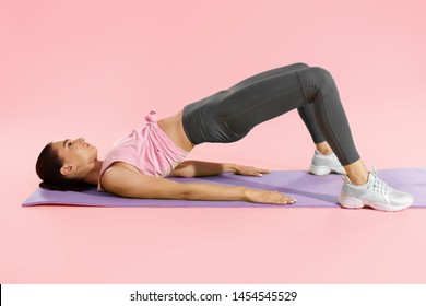 Fitness Woman Doing Hip Workout Exercise On Yoga Mat At Studio. Full Length Shot Of Fit Girl Model In Sportswear Exercising, Doing Pelvic Muscle Exercises On Pink Background