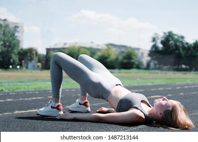 Fitness Woman Doing Hip Workout Exercise On A Stadium. Fitness Girl In Sportswear Exercising, Doing Pelvic Muscle Exercises 