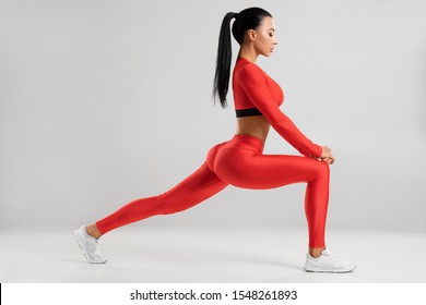 Fitness woman doing lunges exercises for leg muscle workout training. Active girl doing front forward one leg step lunge exercise, on the gray background