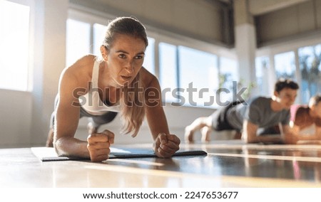 Fitness woman doing plank exercise workout in a group of people in gym. Sport girl and men in sportswear doing exercising on yoga mat, planking indoors