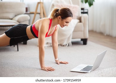 Fitness woman doing push-up exercise and watching online workout session on laptop, training in living room - Shutterstock ID 1739154959