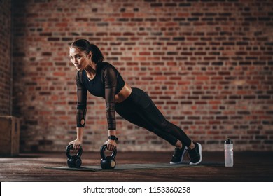 Fitness woman doing pushups with kettle bell at gym. Female athlete doing cross training at gym.
