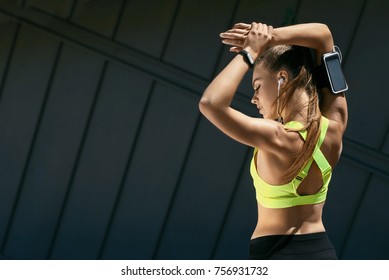 Fitness. Woman Doing Workout Exercise On Street. Beautiful Girl With Fit Body In Stylish Sportswear With Sports Devices Listening Music While Stretching Arms Outdoors. High Resolution