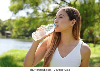 Fitness woman drinking water from bottle. Brazilian Caucasian female drinking water after exercises or sport in the park. - Powered by Shutterstock