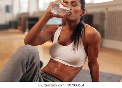 Fitness woman drinking water from bottle. Muscular young female at gym taking a break from workout. - Powered by Shutterstock