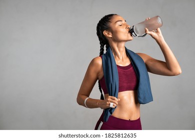 Fitness woman drinking water standing on gray background with copy space. Portrait of sweaty latin woman take a break after intense workout. Mid adult lady drink from water bottle after gym workout.  - Powered by Shutterstock