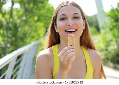 Fitness Woman Eating An Energy Bar Looking At Camera. Close Up Of Sporty Girl Eating A Cereal Snack Outdoor.