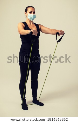 fitness woman with elastic bands doing front shoulders with mask