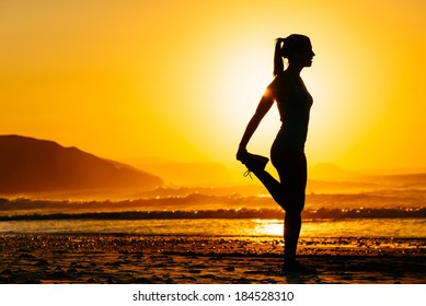 Fitness woman exercising and stretching legs on beautiful summer sunset or morning at beach. Female runner warming up or cool down.
