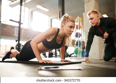 Fitness Woman Exercising With Fitness Trainer In Gym. Woman Doing Push Ups Exercise With Her Personal Trainer At Health Club.