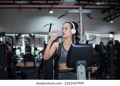 Fitness woman with headphones drinking water while resting on treadmill in gym. Healthy lifestyle concept. - Shutterstock ID 2262437999