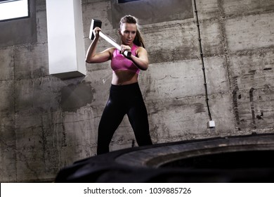 Fitness Woman Hitting Wheel Tire With Hammer Sledge In The Gym.