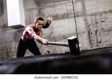 Fitness Woman Hitting Wheel Tire With Hammer Sledge In The Gym.