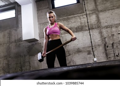 Fitness Woman Hitting Wheel Tire With Hammer Sledge In The Gym.