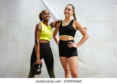 Fitness woman holding kettlebell and standing with her friend in sportswear looking at camera. Portrait of a woman with her fitness trainer.