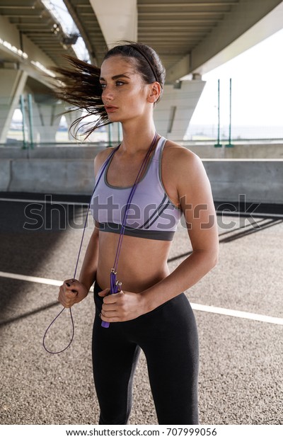 Fitness woman with jump rope under a bridge,\
standing outdoors