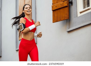 Fitness woman listening music with earphones while running outdoors.Young woman wearing headphones running on sunny day. - Powered by Shutterstock