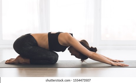 Fitness, woman meditating in child's pose, girl making exercise in light studio over window - Powered by Shutterstock