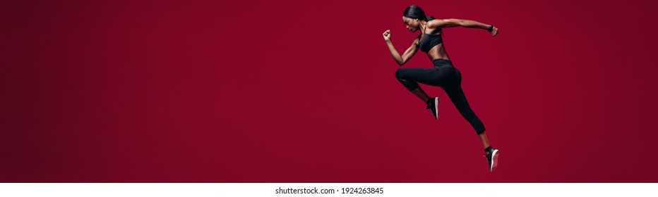 Fitness woman running over red background. Full length shot of strong african woman sprinting on a wide background with copyspace.