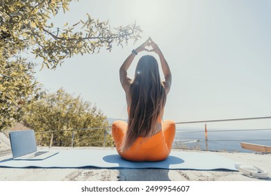 Fitness woman sea. Happy middle aged woman in orange sportswear exercises morning outdoors on yoga mat with laptop in park over ocean beach. Female fitness pilates yoga routine. Healthy lifestyle. - Powered by Shutterstock