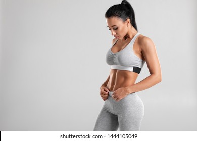 Fitness woman showing abs and flat belly, isolated on gray background. Beautiful athletic girl, shaped abdominal