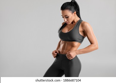 Fitness woman showing abs and flat belly, on gray background. Beautiful athletic girl
