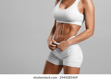 Fitness woman showing abs and flat belly, isolated on gray background. Beautiful athletic girl, shaped abdominal