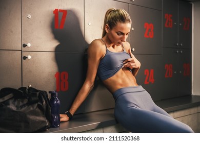 Fitness Woman Showing Her Flat Stomach While Resting In Locker Room After Hard Training At The Gym.