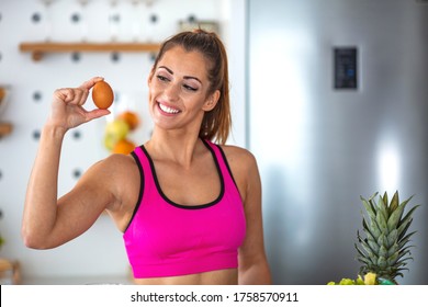 A Fitness Woman Is Showing Off Chicken Eggs. She Stands With Them In Her Hands And A Kitchen In The Background. Smiling Woman Holding Egg. Fitness Woman Prepare Healthy Breakfast.