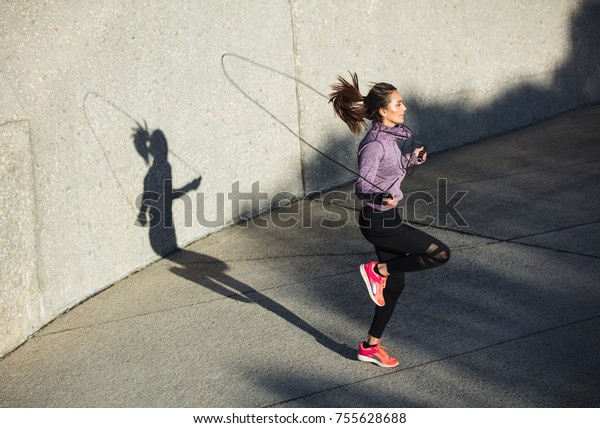 Fitness woman skipping with a jump\
rope outdoors. Female doing fitness training in\
morning.
