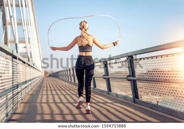 Fitness woman\
skipping the rope on the bridge.\
