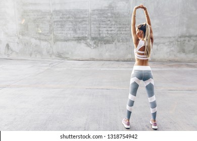 Fitness woman in sportswear doing stretching exercise on the city street over gray concrete background. Outdoor sports clothing and shoes, urban style.