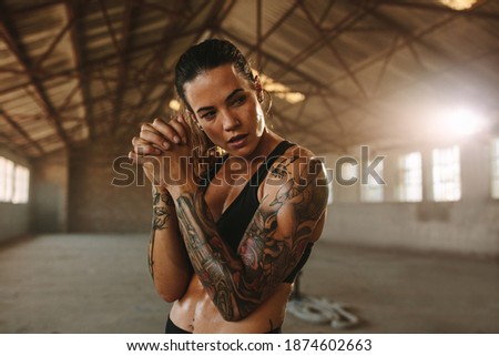 Fitness woman standing inside old factory. Tattooed woman after workout session in old warehouse.
