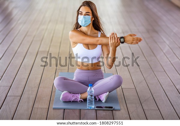 Fitness\
woman stretching outdoor with a face mask. One young woman doing\
stretching exercises and wearing a mask. Woman with a protective\
face mask stretching and exercising\
outdoors