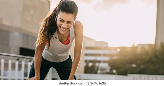 Fitness woman taking a break during the running workout in the city. Fit female athlete smiling and leaning on her knees after morning training session. - Powered by Shutterstock