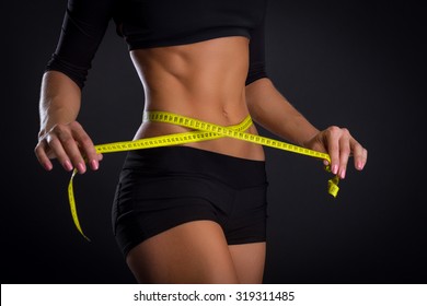 Fitness Woman With Tape Measure Showing Her Waist On Black Background