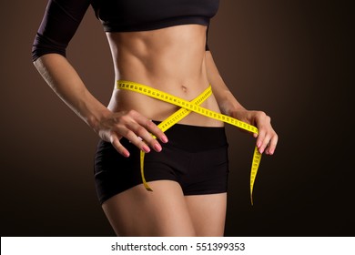 Fitness Woman With Tape Measure Showing Her Waist Isolated On Brown Background