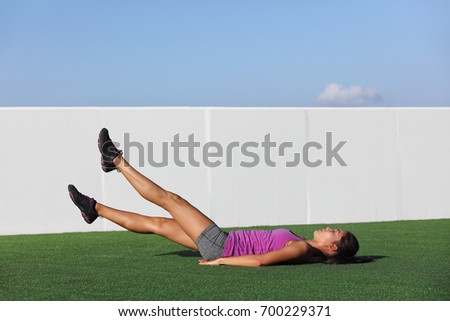 Fitness woman training abs workout doing scissor lifts leg raise or flutter kicks exercise out outdoor grass floor at gym.