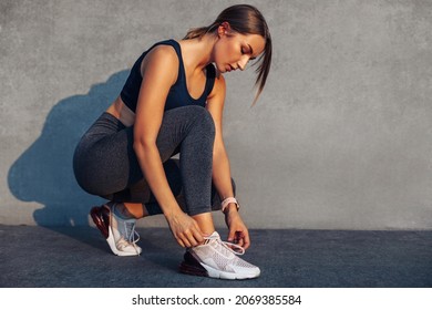 Fitness woman tying shoelaces before training, Cheerful runner sits on the floor in the street in sports shoes, Active woman tying lace shoes before jogging