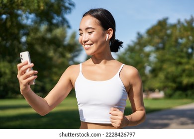 Fitness woman with water bottle and smartphone, jogging in park and smiling, looking at her mobile phone app, checking sport application. - Powered by Shutterstock