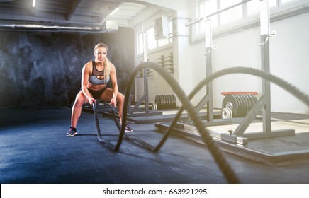 Fitness woman working out with battle rope at gym
