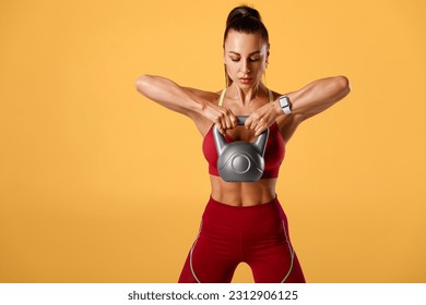Fitness woman working out with kettlebell on orange background. Athletic girl doing exercise for delt