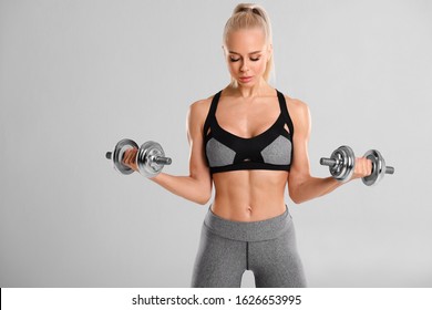 Fitness woman workout with dumbbells on gray background. Athletic girl doing exercise for biceps.