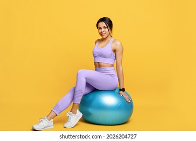 Fitness workout concept. Happy slim african american lady sitting on fitball and smiling to camera, posing over yellow background, studio shot