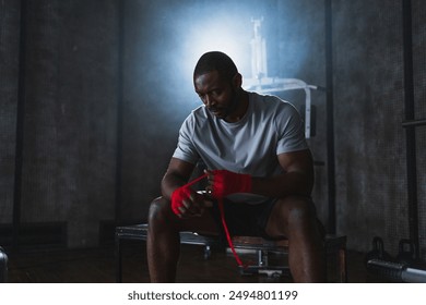 Fitness workout in gym. African American man fighter preparing for fight wrapping hands with red boxing wraps sports protective bandages in gym. Strong man ready for fight boxing sparring training - Powered by Shutterstock