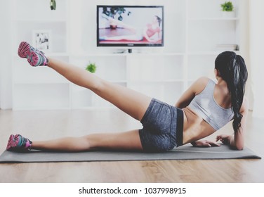 Fitness, Workout, Healthy Living And Diet Concept.  Rear View Of Young Woman Is Stretching On Floor And Watching Tv At Home.