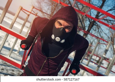 Fitness Workout Outdoors. Male Muscular Man Wearing Training Mask Doing Exercises On Parallel Bars In Winter.